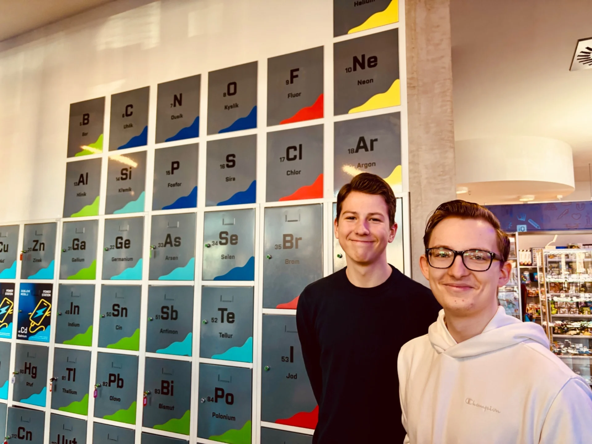 Bild: zwei Schüler lächeln, im Hintergrund ein Teil des Periodensystems