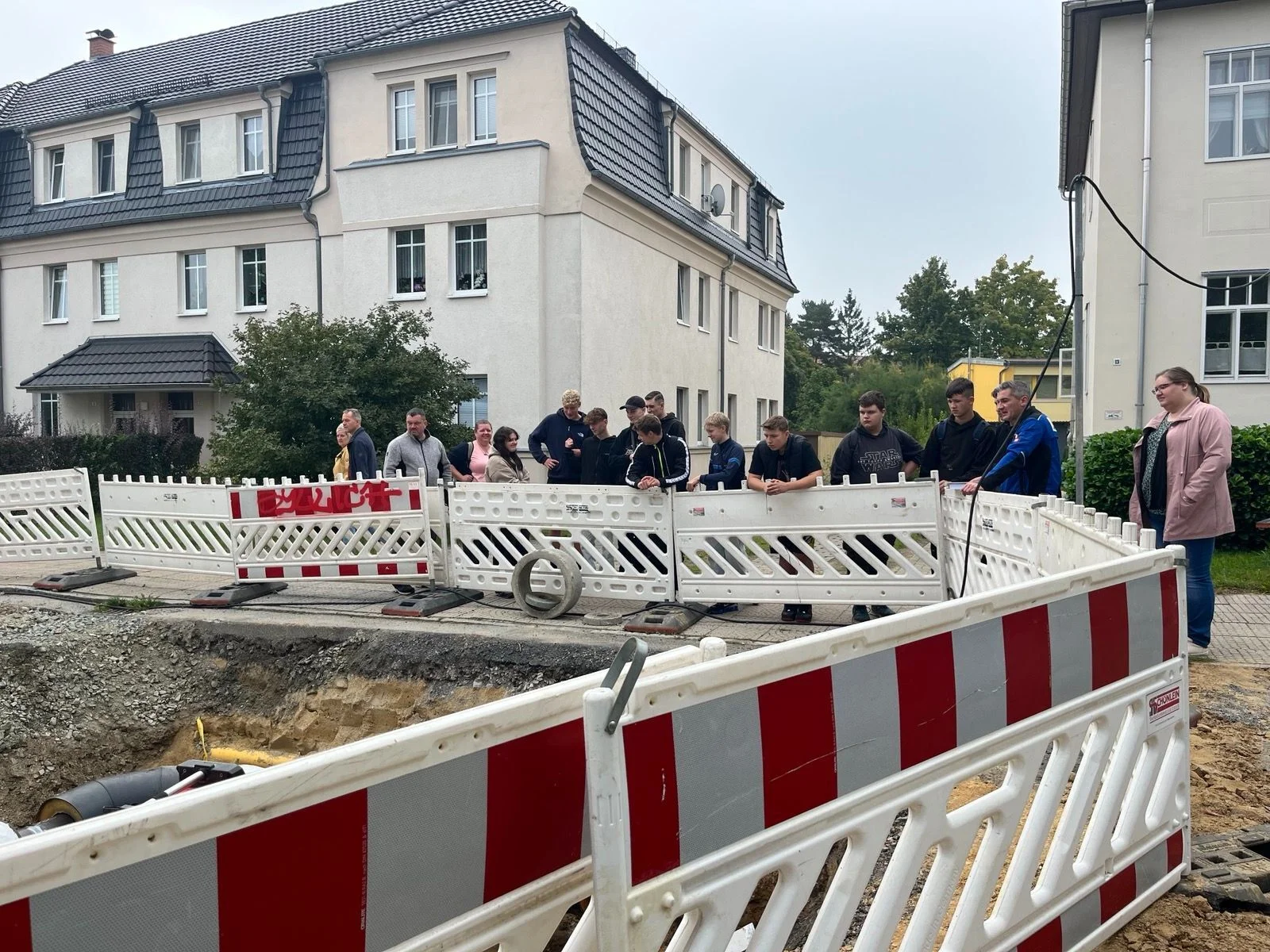 Bild: Schülergruppe steht hinter einer Straßenabsperrung und schaut auf eine große Baustelle