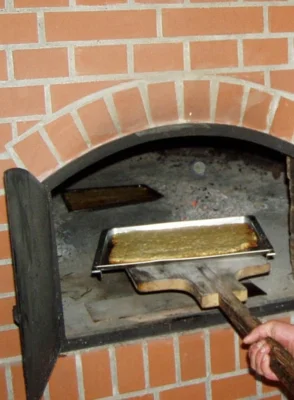 Mit einen Schieber wird ein Blech frisch gebackener Kuchen aus dem Backofen geholt.