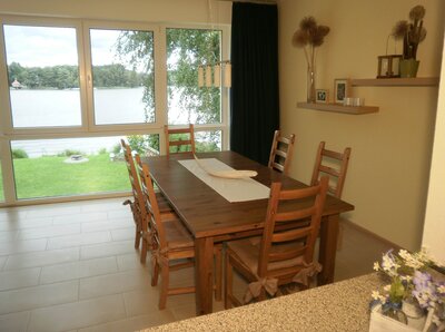 Vorschaubild: Neben der Sitzgruppe mit Couchtisch steht ein großer Esstisch im kombinierten Schlaf-, Wohn- und Esszimmer mit Ausblick auf den See zur Verfügung.