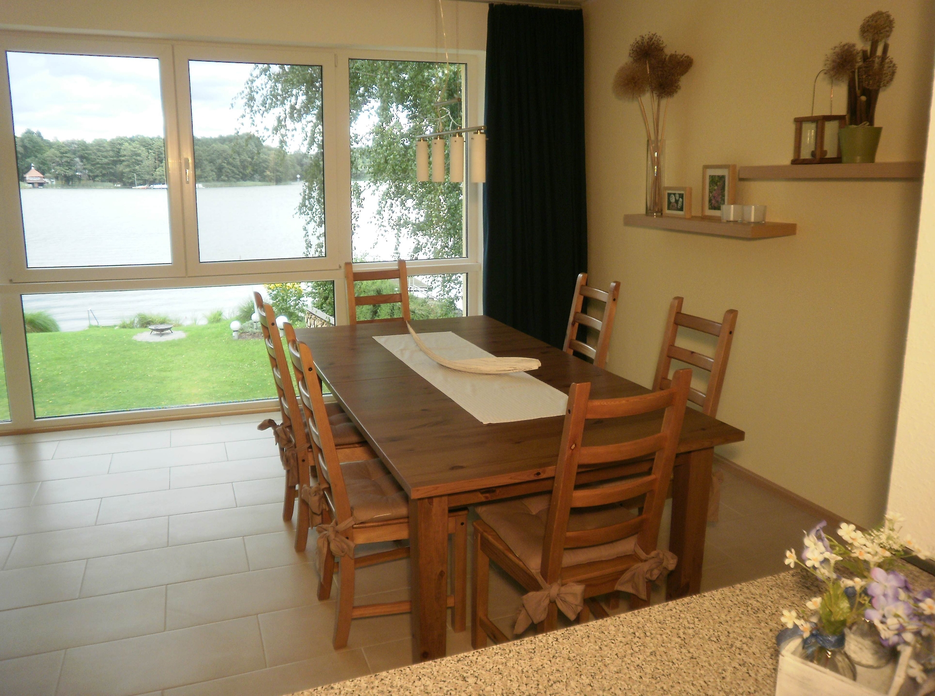 Neben der Sitzgruppe mit Couchtisch steht ein gro&szlig;er Esstisch im kombinierten Schlaf-, Wohn- und Esszimmer mit Ausblick auf den See zur Verf&uuml;gung.  (Bild vergr&ouml;&szlig;ern)