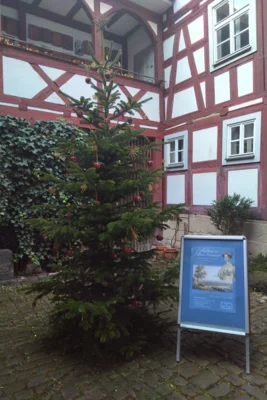 Weihnachtsbaum geschmückt mit Strohsternen und Äpfeln im Innenhof des Stadtmuseums, daneben ein Plakat zur aktuellen Sonderausstellung (Bild vergr&ouml;&szlig;ern)