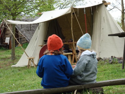 Zwei Kinder in mittelalterlicher Kleidung sitzen im Freilichtmuseum "Stary lud".