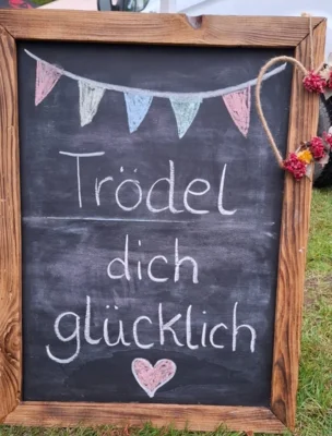 Auf einer alten Tafel steht mit Kreide geschrieben der Spruch "Trödel dich glücklich". (Bild vergr&ouml;&szlig;ern)