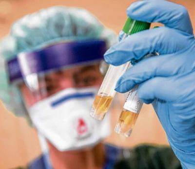 Eine Krankenschwester auf einer Infektionsstation betrachtet in Schutzkleidung und mit einer Atemmaske zwei Abstrichröhrchen. Foto: Bernd Thissen/dpa