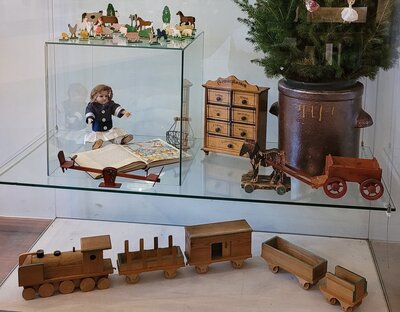 Altes Spielzeug, zum Beispiel eine Holzeisenbahn, ein Püppchen und eine kleine Pferdekutsche, stehen in einer Vitrine im Heimatmuseum Dissen.