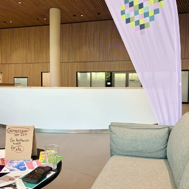 Das Café im oberen Foyer des Stadtforums, die Wände sind aus Holz, es stehen Pflanzen und Sofas im Raum. Auf einem Tisch liegen bunten Karte von Inklusion vor Ort, dahinter steht die Fahne vom Projekt.
