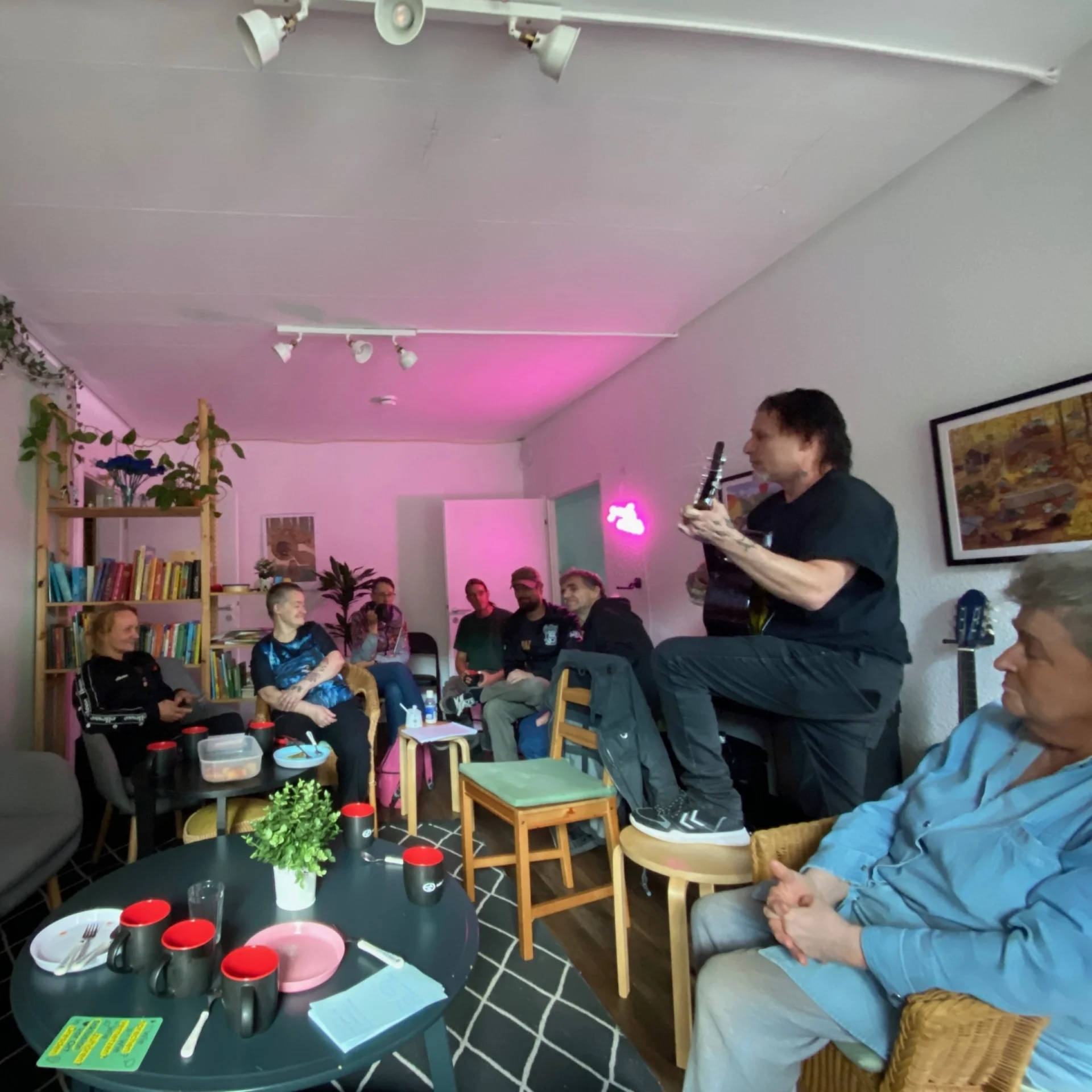 Ein Raum im Treff des Roten Baums, es ist ein Zimmer. Viele Menschen sind darin, ein Mensch spielt Gitarre