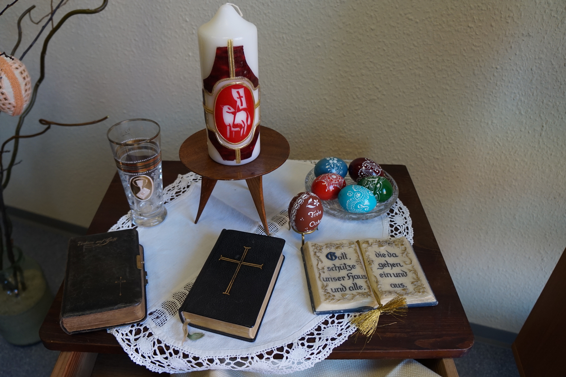 Bild: christlicher Ostertisch mit Osterkerze, Gesangbüchern und Konfirmationsbecher