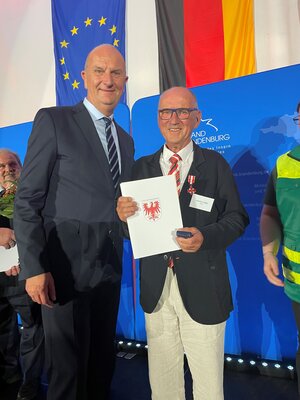 Ministerpr&auml;sident Dietmar Woidke &uuml;berreicht die Auszeichnung an Joachim Liedke, Notfallseelsorger aus L&uuml;bbenau/Spreewald. (Foto Landkreis)  (Bild vergr&ouml;&szlig;ern)