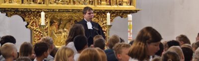 Unser Pastor erz&auml;hlt, dass Jesus ganz besonders die Kinder liebt und all ihre Talente sch&auml;tzt. Wir stellen unsere neuen Mitsch&uuml;lerinnen und Mitsch&uuml;ler unter den Schutz Gottes.  (Bild vergr&ouml;&szlig;ern)