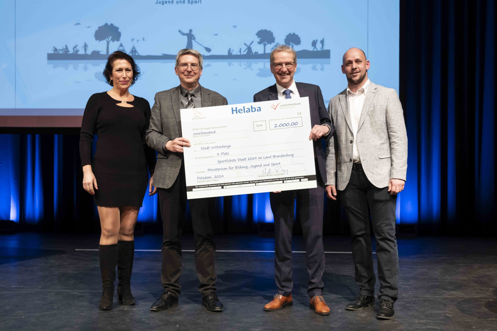 Bild: Henrik Fischer, Staatssekretär im Ministerium für Bildung, Jugend und Sport des Landes Brandenburg (2.v.r), und Kristy Augustin, Vizepräsidentin für Breitensport und Sportentwicklung beim Landessportbund, überreichten einen Scheck über 2.000 Euro an Bürgermeister Dr. Oliver Hermann und Tino Gerloff (r) vom Kreissportbund