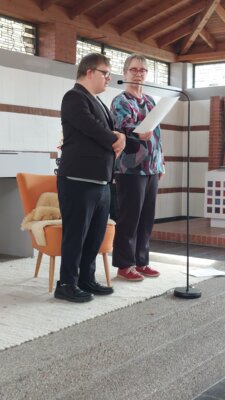 Kirsten Erhardt und Henri Hirt stehen gemeinsam vor dem Publikum. Henri Hirt liest vor. 