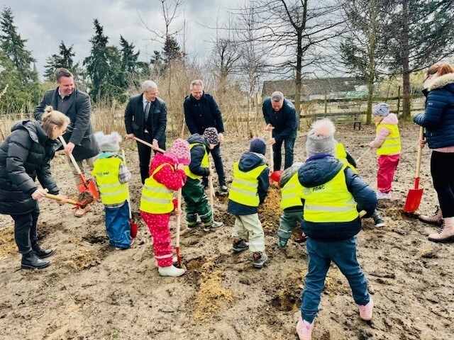 Bild: Die Kita-Kinder der bisherigen Kita in Dabergotz helfen beim Spatenstich kräftig mit. Dazu hat die Sparkasse den Kindern rote Kinderspaten organisiert. Gemeinsam buddeln sie mit Sparkassen-Vorstand, DRK-Kreisverband, Landrat und Amtsdirektor.