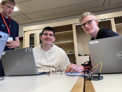 Sch&uuml;ler:innen sitzen am Laptop, im Hintergrund ein Azubi von Trumpf-H&uuml;ttinger  (Bild vergr&ouml;&szlig;ern)