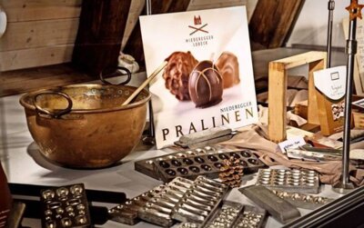 Vorschaubild: Xocolatl – die bitter – süße Verführung von Wolfgang Berger Das Stadtmuseum Wendlingen widmet sich mit einer Ausstellung der Geschichte von Kakao und Schokolade. Schon der Azteken-König Montezuma schwörte auf die kleine braune Bohne. Aus dem Grundstoff lassen sich feinste Leckereien zaubern. Dass Schokolade glücklich machen soll, ist hinlänglich bekannt. Deshalb ist es auch keine große Überraschung, dass im Stadtmuseum Wendlingen empfohlen wird, den Genuss von Schokolade ganz oben auf der täglichen To-do-Liste zu haben. Doch die aktuelle Ausstellung „Xocolatl – auf den Spuren der Schokolade“ liefert auch reichlich weniger bekannte Informationen, die einen staunen lassen. So hatte beispielsweise der Azteken-Herrscher Montezuma im 15. Jahrhundert einer Überlieferung spanischer Konquistadoren zufolge eine wohl besonders große Schwäche für die kleine braune Kakaobohne. Der letzte König der Azteken soll sich „täglich bis zu 50 Becher – goldene Schalen – des dunklen herben Getränkes“ einverleibt haben, heißt es im Wendlinger Ausstellungstext. „Xocolatl“ – schon der Name deutet auf einen fernen Ursprung hin. „Bitteres Wasser“ oder „Kakaowasser“ – so die Übersetzung – kannten die Ureinwohner Mittelamerikas früh als Nahrungs- und Genussmittel. Schon die Olmeken, die circa zwischen 1500 vor bis 300 nach Christus im fruchtbaren Tiefland des Golfs von Mexiko siedelten, kannten den Kakao. Einem Mythos zufolge brachte der Gott der Winde, Quezalcoatl, den Samen der Kakaopflanze den Menschen, damit sie daraus das „Getränk der Götter“ zubereiten konnten. Im Krieg blieb Schokolade den Soldaten vorbehalten Der Eroberer Hernando Cortez erkannte zu Beginn des 16. Jahrhunderts als erster Europäer die Bedeutung der exotischen Frucht. Aus der Neuen Welt traten Kakao und Schokolade schließlich den Siegezug um die Welt an und erfreuten sich auch in Deutschland rasch wachsender Beliebtheit. Anfang des 20. Jahrhunderts ging der Boom der Schokoladenindustrie ungebremst weiter. „1914 gab es bereits 180 Schokoladenfabrikanten. Innerhalb weniger Jahre kam es zur Verdopplung von Kakaoanbau und Konsum“, erfährt der Besucher im Stadtmuseum Wendlingen. Einen Einschnitt in der Versorgung bedeutete der Erste Weltkrieg. Lieferungen fielen aus, und „im Dezember 1916 wurden alle Vorräte für das Heer eingezogen“. Ähnliches wiederholte sich dann auch im Zweiten Weltkrieg. Von 1940 an gab es keine Schokolade mehr für den privaten Konsum. „Die gesamte Produktion ging an das Militär“. Dafür stellten wie schon im Ersten Weltkrieg die Schokoladenfabriken zwangsweise erneut Grundnahrungsmittel und Ersatzstoffe her. Als dann die Amerikaner als Besatzungsmacht nach Deutschland kamen, hatten sie auch Schokolade im Gepäck. Manche Großeltern erinnern sich noch an damals, wie sie als Kinder mit glänzenden Augen ein Stück Schokolade aus den Händen eines GI empfingen. Die Milka-Kuh Adelheid lässt grüßen Die interessante Ausstellung zieren zahlreiche Exponate, wie beispielsweise Schokoladenhasen und Tafelschokolade bekannter Marken wie Lindt, Cailler oder Ovomaltine. Auch Adelheid – die erste Milka-Kuh – lässt grüßen. Utensilien wie Marzipanzangen, Verziergabeln, Kakaotöpfe oder Schoko-Quirle dienen als Anschauungsobjekte bei der Erklärung des Herstellungsprozesses von Schokolade. Nicht nur geschichtliche Hintergründe bietet die Ausstellung, sie ist auch didaktisch ansprechend aufbereitet. Ein Filmbeitrag der Sendung „Willi wills wissen“ etwa erklärt Kindern die süße Welt der Schokolade altersgerecht. Und die Schau verschweigt auch nicht „die bittere Wahrheit über Schokolade“. Der Besucher erfährt, dass Millionen von Kleinbäuerinnen und –bauern oft unter menschenunwürdigen Bedingungen den Kakao für unsere Schokolade produzieren. Er lernt aber auch, wie er durch den Kauf von fair gehandelten Produkten dem entgegentreten kann.