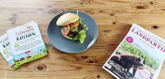 Bild: Plakate zur Katerbower Landpartie, der Temnitz-Burger und die Broschüre zur Brandenburger Landpartie 2025 der pro agro auf einem Tisch
