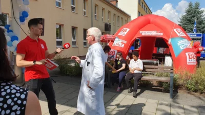 BB Radio Moderator und Chefarzt Dr. Schult mit Radiopavillon und G&auml;sten im Hintergrund 