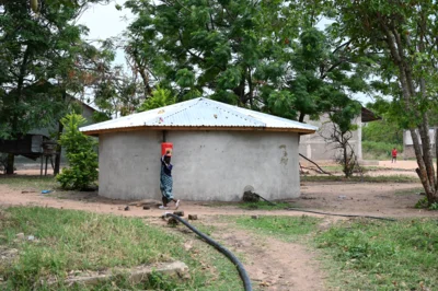 Ein Rundbau aus Ziegeln, verputzt, mit Wellblechdach und Pumpe versehen - der neue Wassertank.  (Bild vergr&ouml;&szlig;ern)