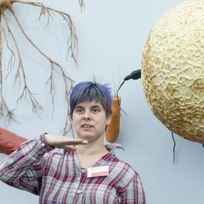 Eine Person mit blauen Haaren zeigt ein Objekt in der Ausstellung des Hygiene-Museums.