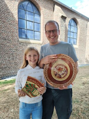 Der Referent Simon Matzerath mit seiner Tochter Marta vor der Alten Kirche Körrenzig. In der Hand in Glimbach produzierte Keramik aus dem 17. und 18. Jahrhundert.