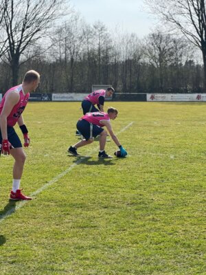 Drei Spieler der Waldenau Kraken in pinkfarbenen Trikots stehen in der Offense-Formation bereit. Der Center hält den Football zum Snap bereit, die Mitspieler sind fokussiert und blicken zum Quarterback. Die Szene wirkt ruhig und konzentriert.