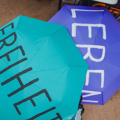 Zwei farbenfrohe, geöffnete Schirme zeigen die Worte „Freiheit“ und „Leben“ – offen, einladend und voller Bedeutung.