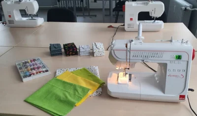 Nähmaschine, Stoffe und Garne sind auf einem Tisch zu sehen
