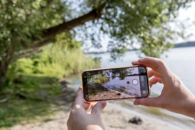 Zwei Hände halten ein Mobiltelefon mit einem Foto von Natur auf dem Display.