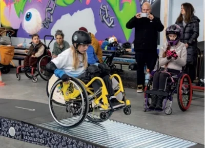Mädchen auf Rollstuhl fährt über eine Rampe