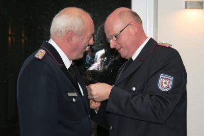 Dirk Lolies (rechts) zeichnet Seesters Wehrf&uuml;hrer Hermann Stieler mit dem Deutschen-Feuerwehr-Ehrenkreuz in Silber aus. 
