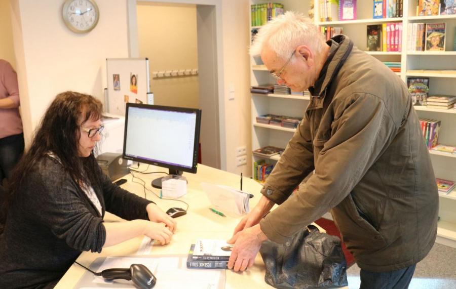 Bild: Mitarbeiterin Anja Voland händigt Norbert Blank den neuen Lesestoff aus. Foto: Stadt Calau / Jan Hornhauer