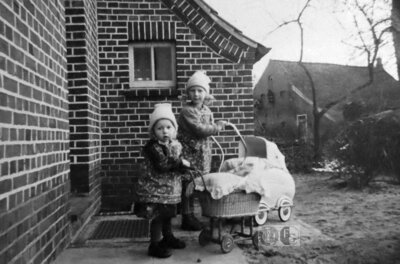 Vorschaubild: In Backemoor machen sich die Schwestern Erfeling mit ihren Puppenwagen in den 1950er Jahren auf den Weg. In ihrem Elternhaus (gleich neben der Molkerei) an der Backemoorer Straße war seinerzeit die Poststelle untergebracht. Im Hintergrund sieht man das Haus der Familie Ewen (Fotoquelle: Mine Oltmanns/Repro: Groeneveld)