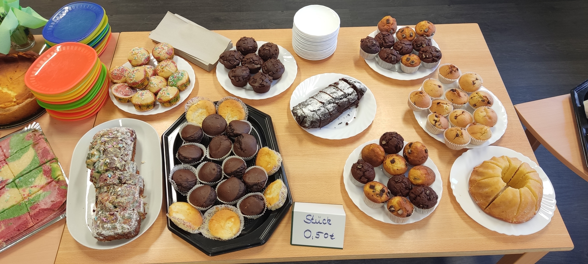 Bild: Ein Tisch mit Kuchen vom Kuchenbasar im Hort. Zu sehen sind neben bunten Tellern auch Rührkuchen und verschiedene Muffins