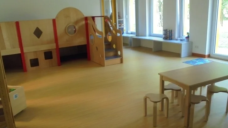 Bild: Der Didaktik-Podestraum bietet den Kindern die Möglichkeit aus einer Vielzahl von Spielen frei nach Interessen zu wählen. Ob beim Puzzeln allein, oder gemeinsam mit anderen Kinder ein Spiel erleben, es werden wichtige Impulse gesetzt. Hier erfahren die Kinder Regeln. Nicht nur Spielregel stehen im Vordergrund, sondern auch Regeln im Umgang mit den Mitspielern. Nicht zuletzt ist die Erfahrung des Gewinnens und des Verlierens unerlässlich. Die zweite Ebene bietet den Kindern eine Möglichkeit von oben auf die Dinge zu schauen. Sie sind größer als die anderen, haben die Möglichkeit andere zu beobachten und werden nicht gleich entdeckt. Es gibt auch die Möglichkeit sich zurückzuziehen, zu verstecken, nicht gesehen zu werden. Kuscheln und Höhle bauen mit den Sitzkissen bieten sich an. Die Musikecke bietet Platz zum Musizieren und Tanzen. Instrumente stehen frei zur Verfügung. Dieser Raum ist den Eltern als Früh-und Spätdienst-Raum bekannt.