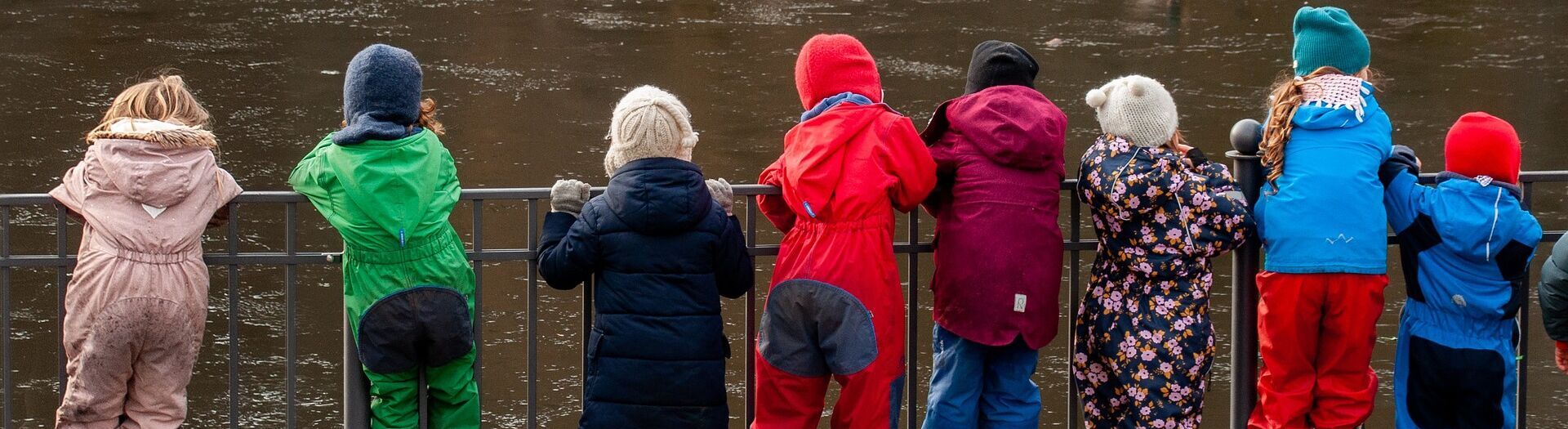 Kindergartenkinder stehen vor einem Geländer und schauen auf einen Teich