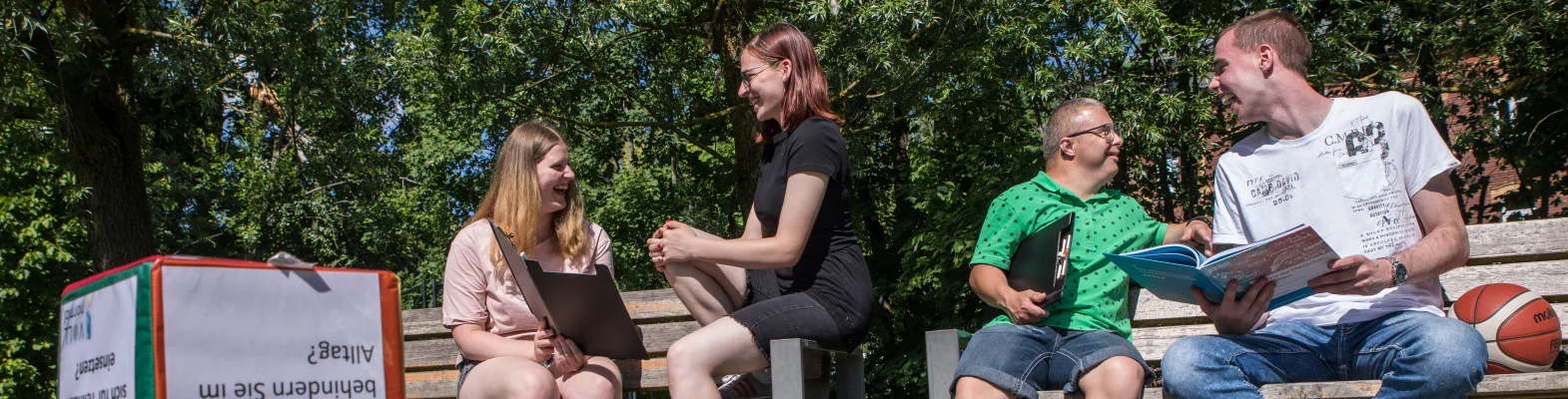 Vier Personen sitzen auf zwei Parkbänken. Sie unterhalten sich und lachen dabei.