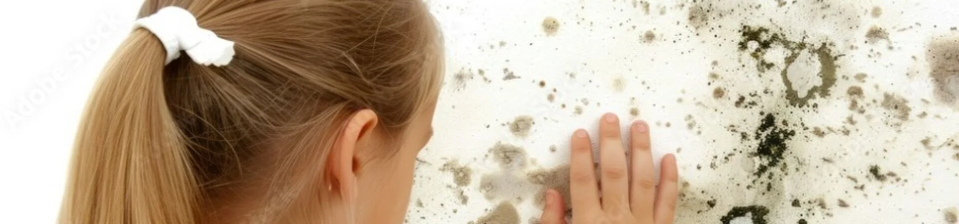 Kind mit blondem Pferdeschwanz berührt eine mit schwarzem und grauem Schimmel befallene Wand. Symbolbild für Schimmelpilz-Allergie und gesundheitliche Belastung.