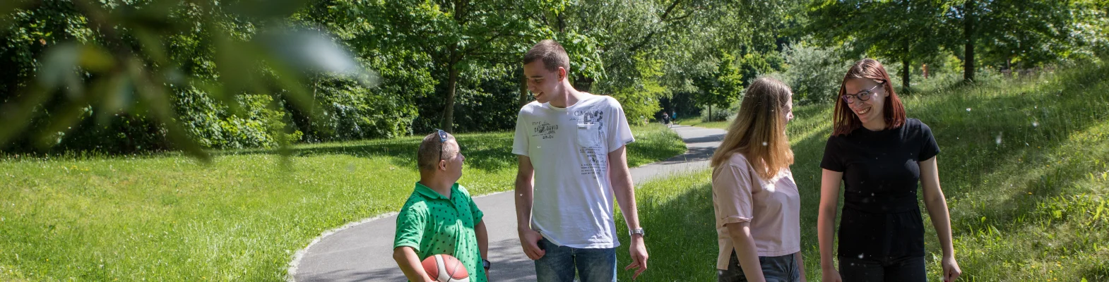 Vier Personen laufen durch den Park und lächeln sich an.