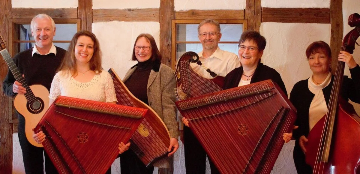 Sechs Personen mit Gitarre, Hackbrett, Zither und Kontrabass lächeln in die Kamera | zur Startseite