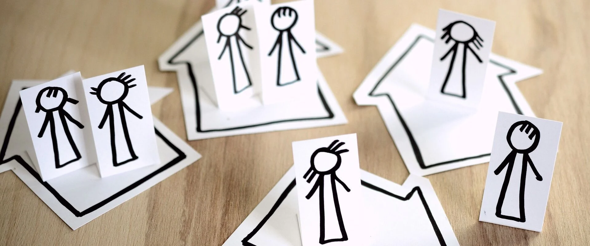 Foto: Papierfiguren stehen auf gezeichneten Häusern. Manche Figuren stehen zusammen in einem Haus und manche alleine.