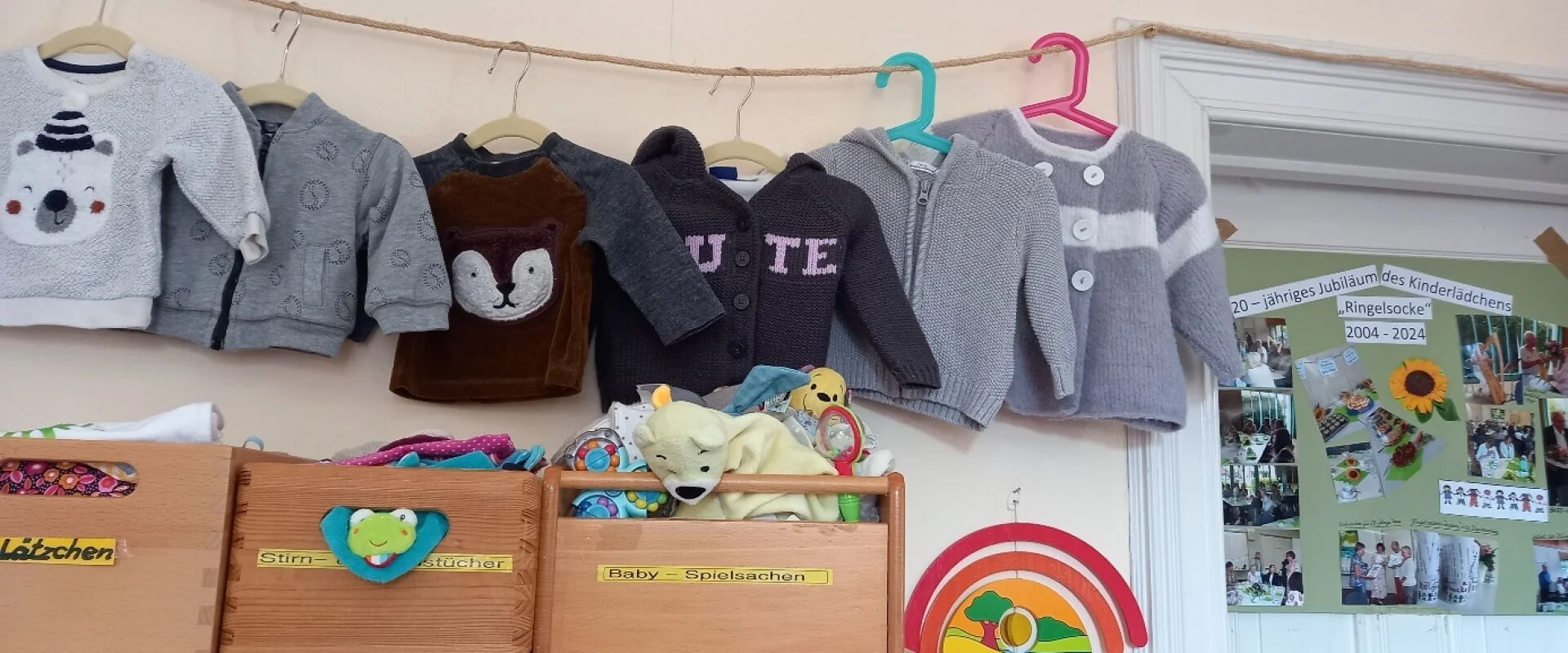 Foto: An einer Leine hängen Pullover und Jacken. Darunter stehen Holzkisten mit Baby-Sachen und Spielzeug.