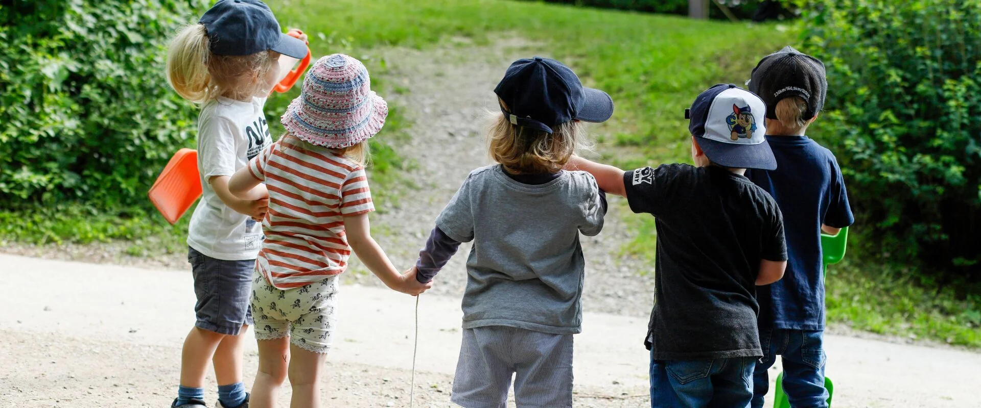 Foto: Fünf Kinder stehen im Halbkreis mit dem Rücken zur Kamera. Sie halten sich an den Händen.