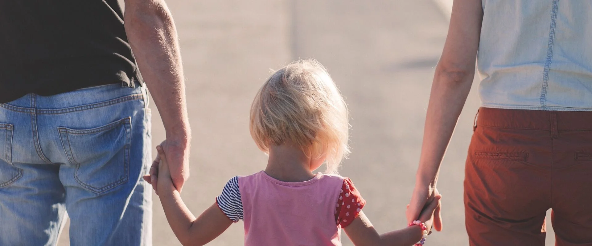Foto: Ein kleines Mädchen geht zischen zwei Erwachsenen und hält ihre Hände