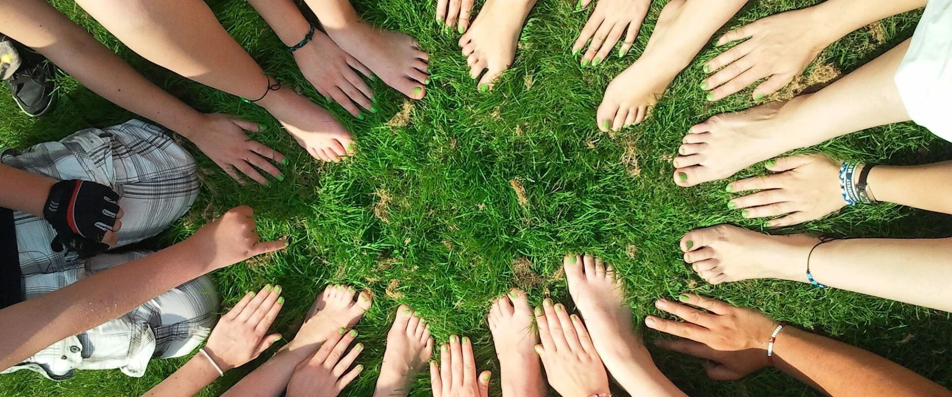 Foto: Viele Menschen bilden einen Kreis aus Füßen und Händen auf einer Wiese.