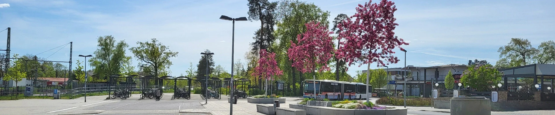Das Foto zeigt den Bahnhofsvorplatz mit Fahrradparkplatz, blühenden Bäumen und einem Bus.