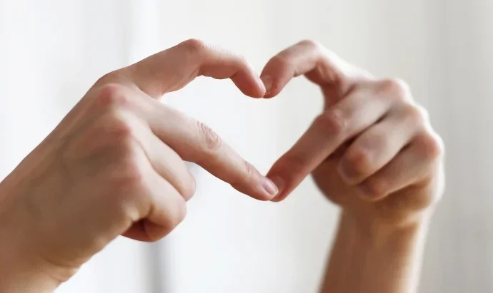 Die Finger von zwei Händen bilden ein Herz.