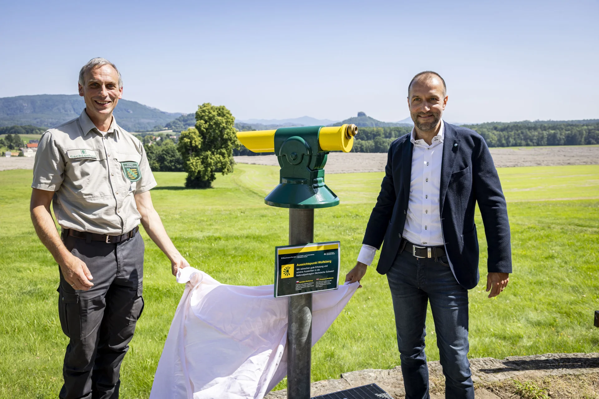 Foto: Marko Förster Der Caspar-David-Friedrich-Weg hat eine neue Attraktion: Ein Fernrohr ermöglicht es, mit einem Schwenk großartige Ausblicke auf die Schrammsteine im Nationalpark und die Kaiserkrone im Landschaftsschutzgebiet zu genießen. Die Übergabe des Fernrohrs an den Bürgermeister von Reinhardsdorf-Schöna, Dr. Andreas Heine (rechts im Bild), durch Daniel Thomann, stellvertretender Leiter der Nationalpark- und Forstverwaltung, fand im Rahmen der Feierlichkeiten statt.