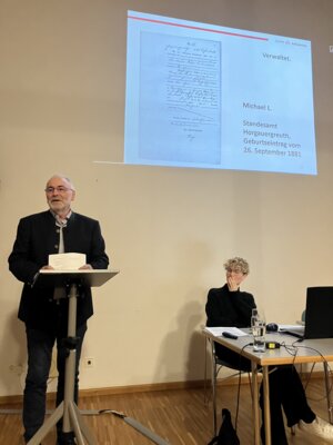 Historiker Dr. Josef Merkl (stehend) von der Stiftung St. Johannes in Schweinspoint und Kathrin Bauer (sitzend) von der Gedenkstätte Schloss Grafeneck / Fotograf: Markt Zusmarshausen (Bild vergr&ouml;&szlig;ern)