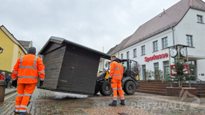 Mitarbeiter des städtischen Bauhofes platzierten am Montag die Holzhütten für den Weihnachtsmarkt auf dem Pritzwalker Marktplatz. Foto: Franziska Liebing/Stadt Pritzwalk (Bild vergr&ouml;&szlig;ern)